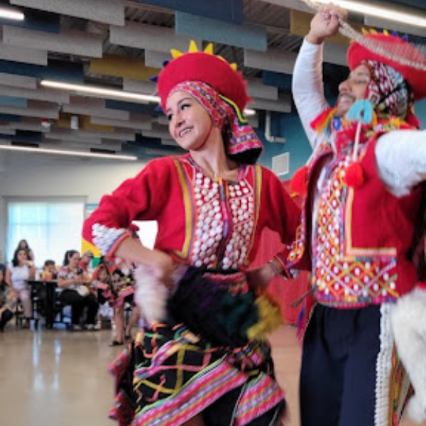 A pair of dancers in colorful traditional clothing performing joyfully one wearing a bright red outfit with intricate patterns smiling while moving gracefully in front of an audience during a cultural celebration