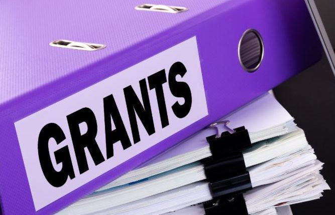 Binder with the word "Grants" on the cover on top of a large stack of papers.