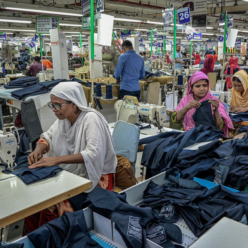 People working at tables with sewing machines inside a factory with cloth material. 