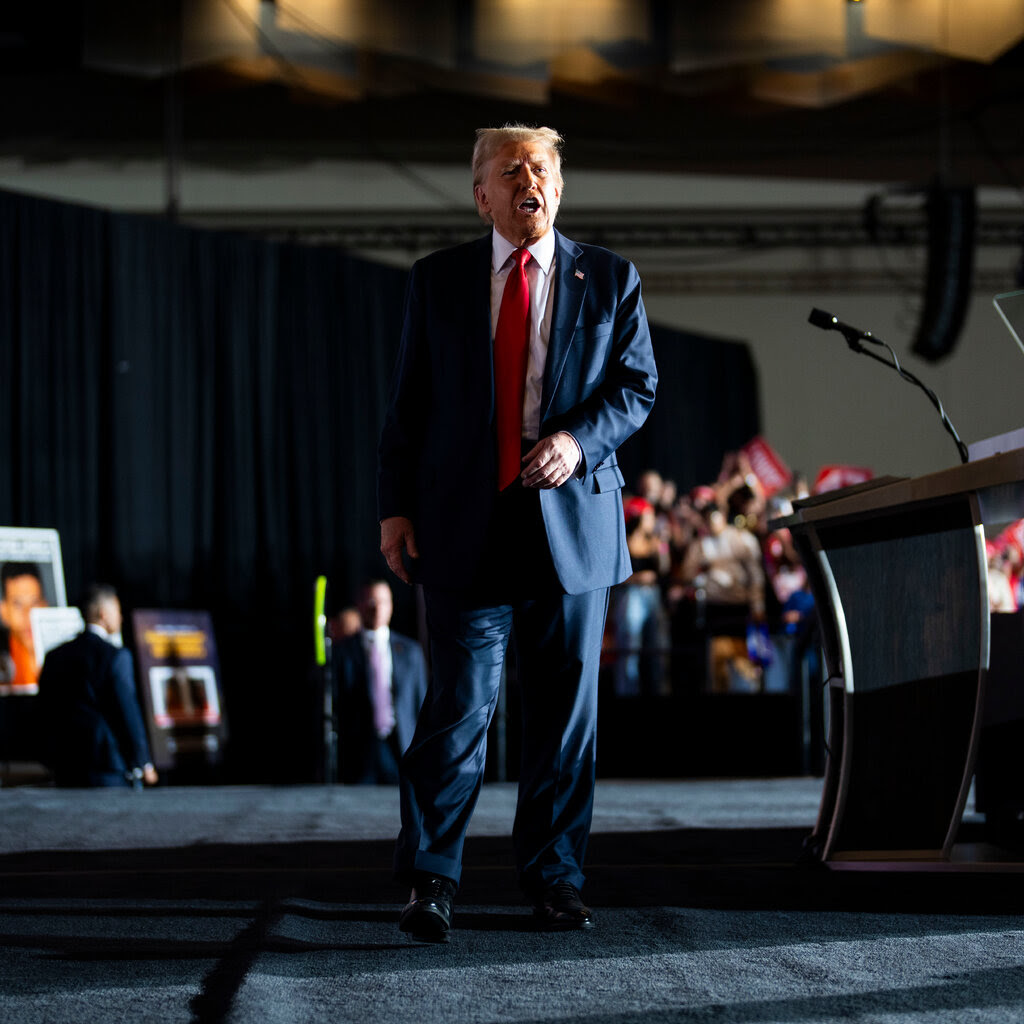 Donald Trump, in a blue suit and a red tie, walks across a stage.