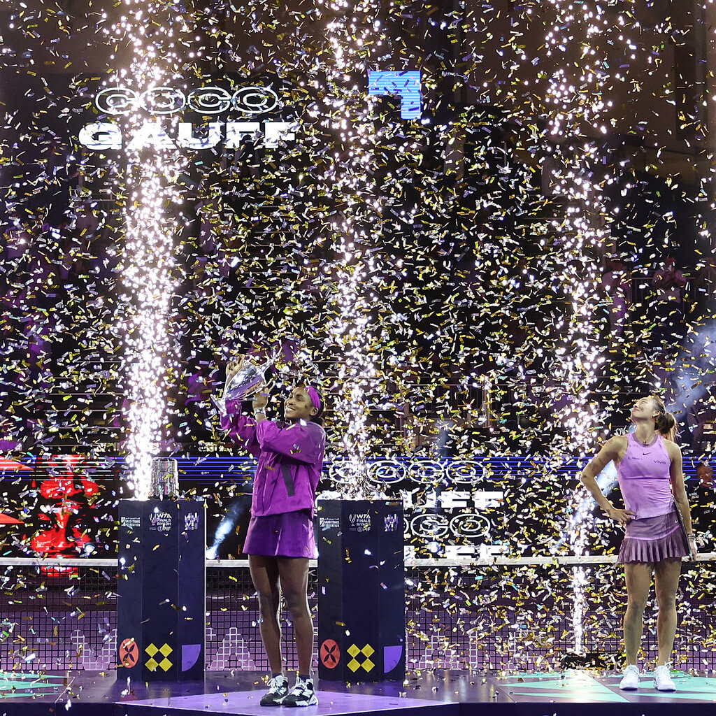 Two tennis players in front of a celebratory display with lights and confetti. One raises a trophy.