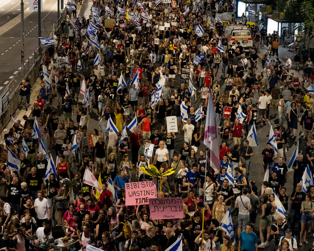 A group of demonstrators on a street seen from above. Many carry Israeli flags.