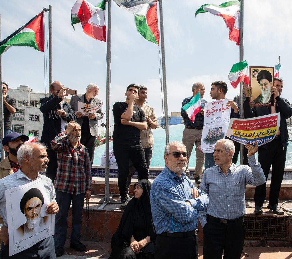 A group of people holding signs of protest against Israel and pictures of Ayatollah Ali Khamenei, the supreme leader, with Iranian flags flying behind them. 
