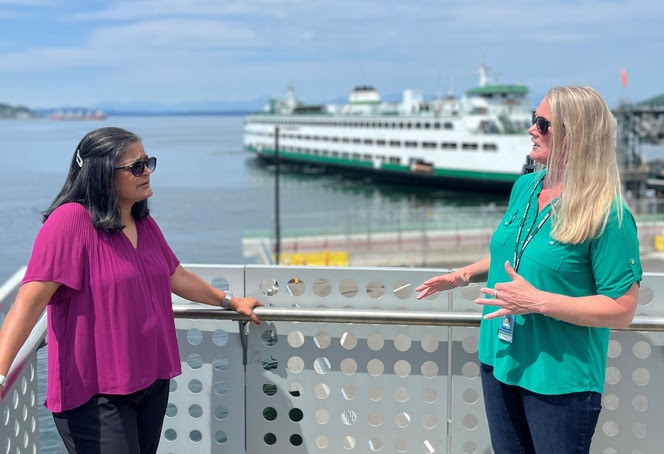 Two people talking at a ferry terminal with a vessel in the background