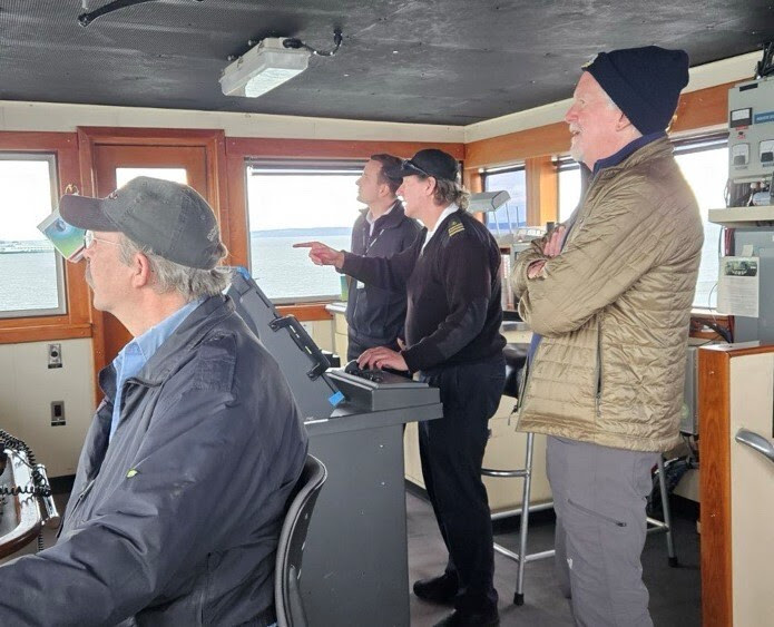Four people in the wheelhouse of a ferry looking out the windows