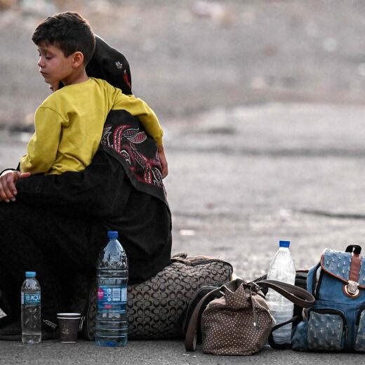 A woman sits with a child on her lap next to bags on the ground as people fleeing from Lebanon arrive on the Syrian side of the border with Lebanon in Jdeidat Yabus in southwestern Syria on September 24, 2024. Israel announced dozens of new air strikes on Hezbollah strongholds in Lebanon on September 24, a day after 492 people, including 35 children, were killed in the deadliest bombardment since a devastating war in 2006. (Photo by LOUAI BESHARA / AFP)