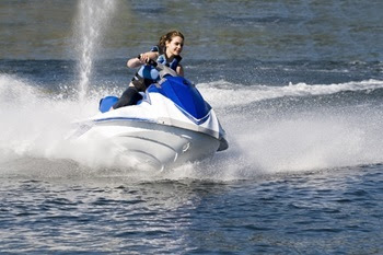 young woman on a blue and white Jet Ski kicks up a foamy wake making a turn on the water