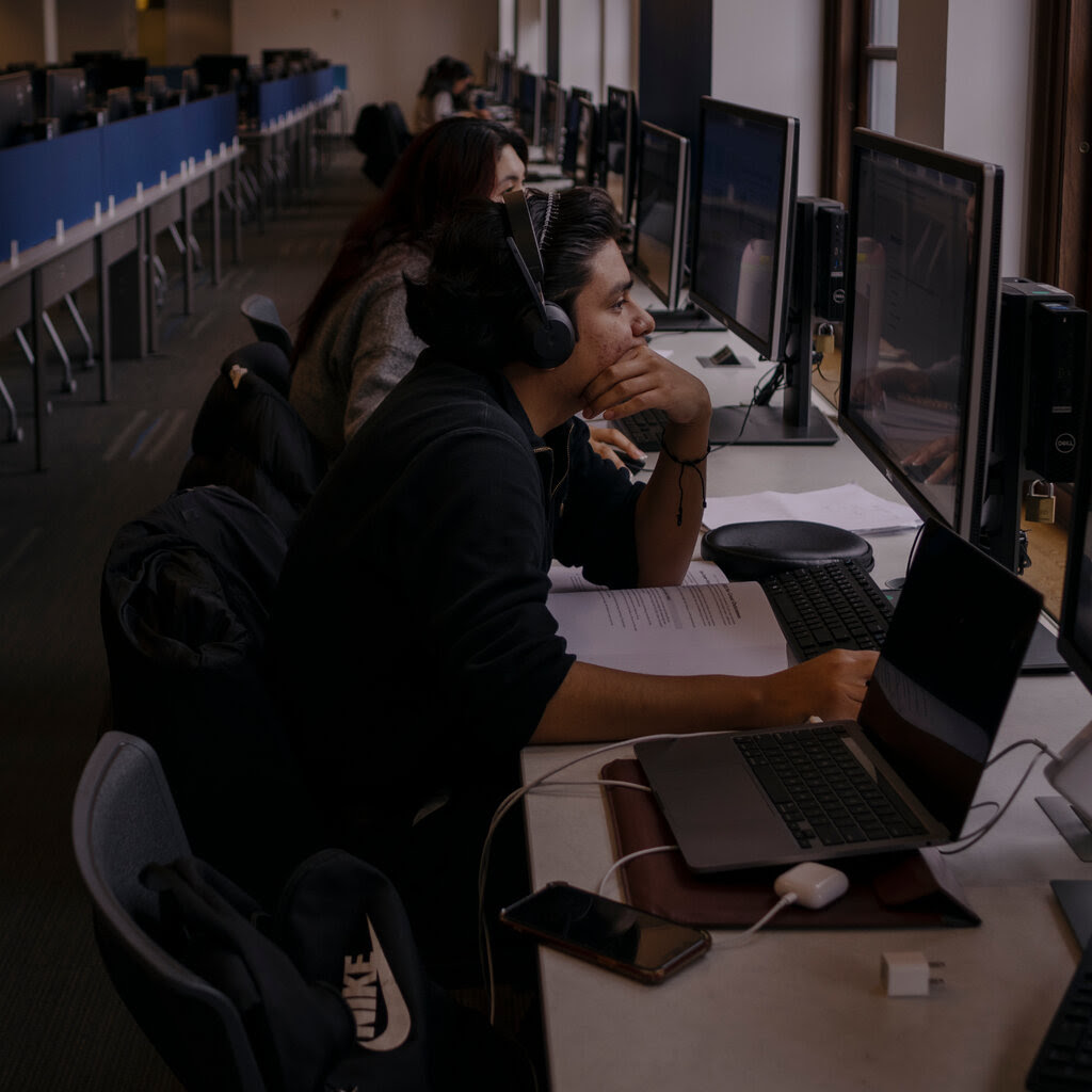 Students sit looking at computers in a row. 