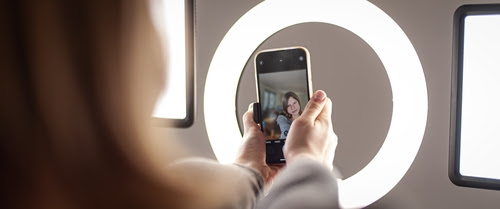 Young woman making photo or video content for social media with smartphone and light of ring lamp. Influencer makes broadcast communicates with followers in social networks. 