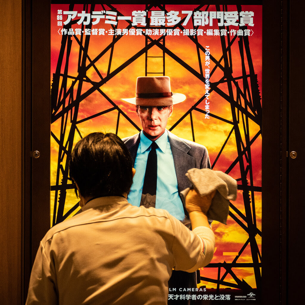 A person cleans the clear casing that covers an advertisement for the movie “Oppenheimer” in Tokyo.