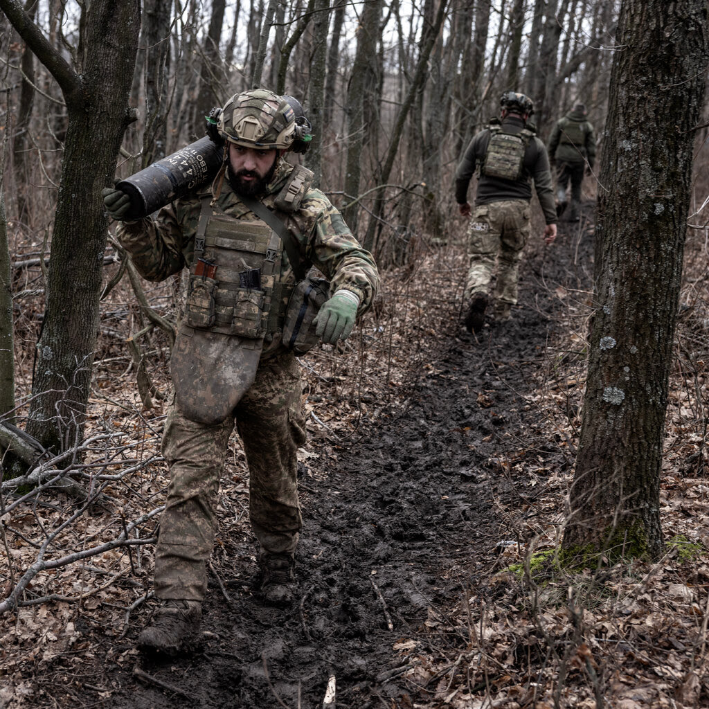 Soldiers in camouflage gear walking through the woods. 