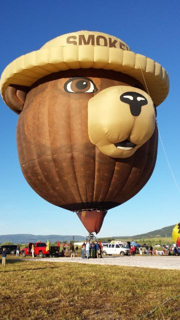 The Smokey Bear Hot Air Balloon is tethered at a site. The balloon looks like Smokey's head, including his iconic ranger hat.
