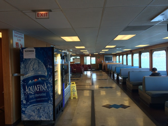 View of interior passenger cabin of a ferry with bench seating along windows and a vending machine visible
