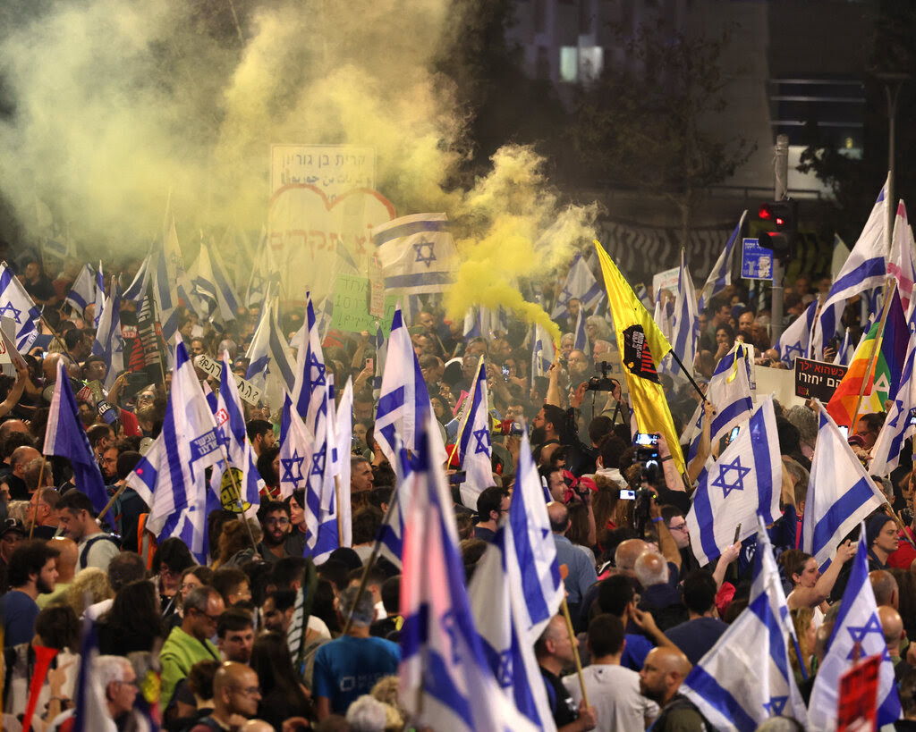 A crowd of people marches with Israeli flags, while yellowish smoke drifts in the air.