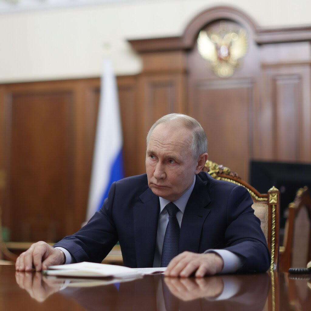 President Vladimir Putin of Russia is seated, and his hands are on the desk in front of him.