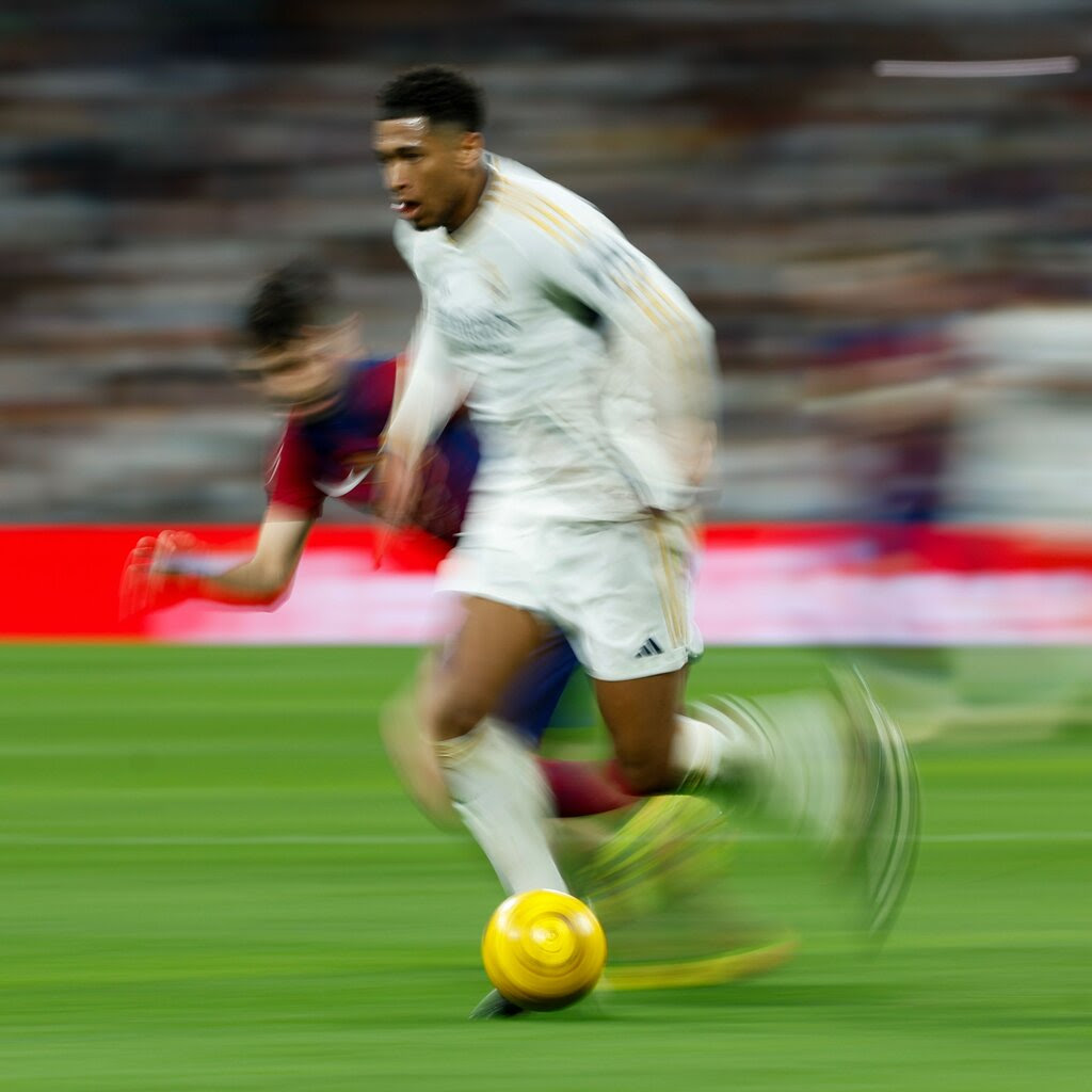 Real Madrid’s Jude Bellingham dribbles a soccer ball past another player. The image is blurry, indicating motion.