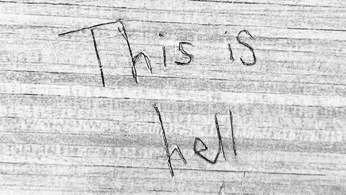 "This is hell" carved into a textured wall.