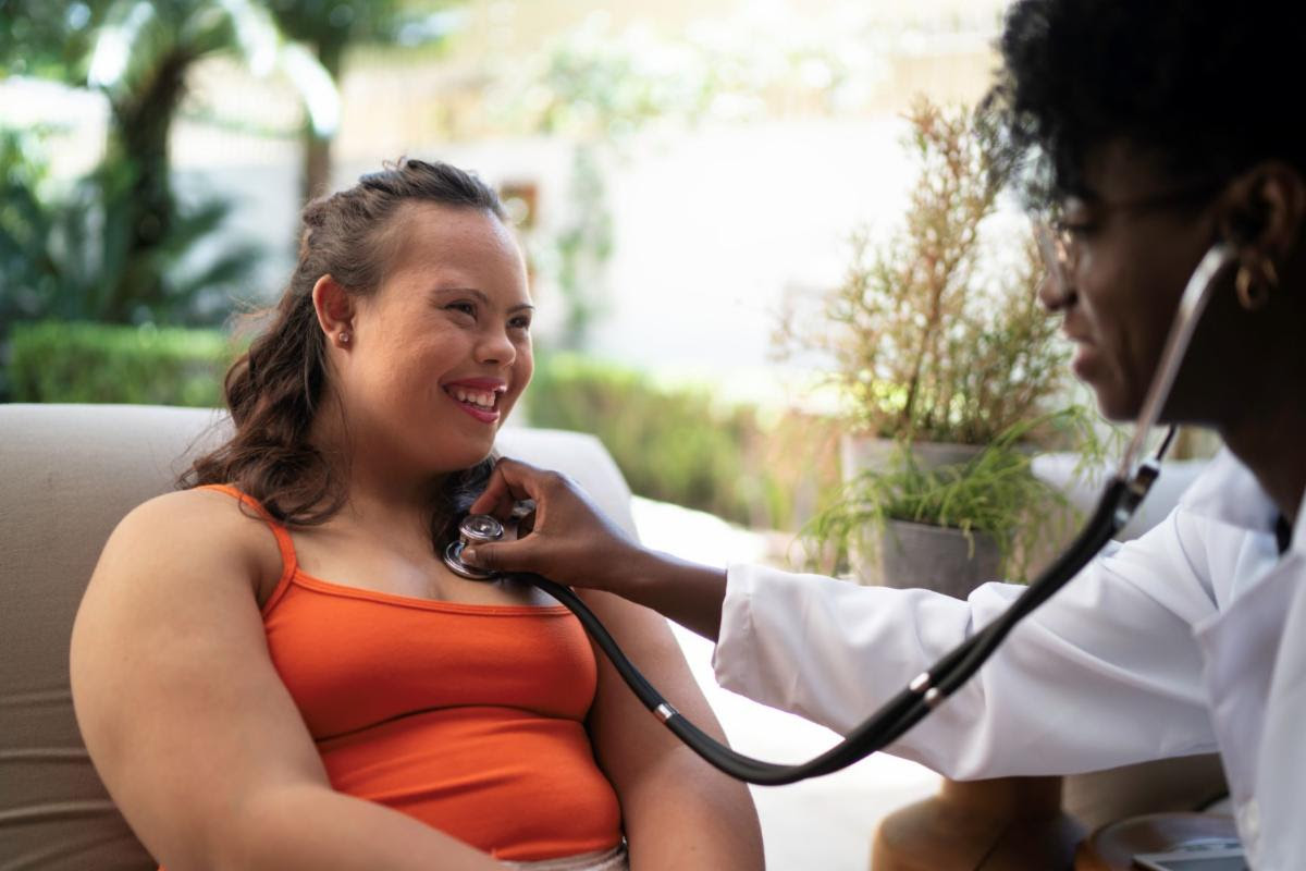 woman patient with down syndrome with Black woman doctor holding a stethoscope to her chest