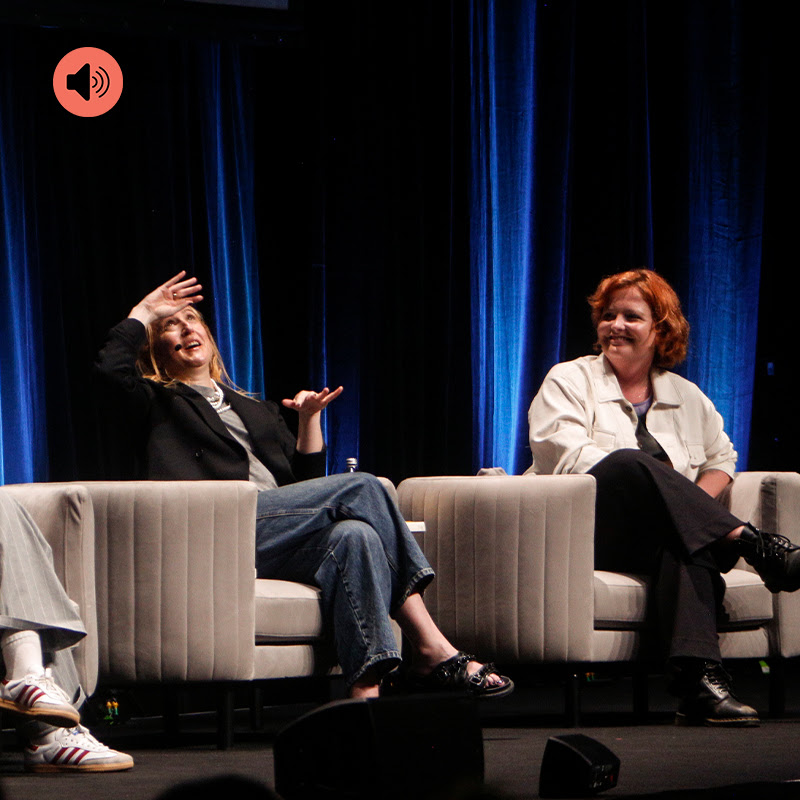 Two people seated on stage talking, with a red podcast icon superimposed in top-left corner