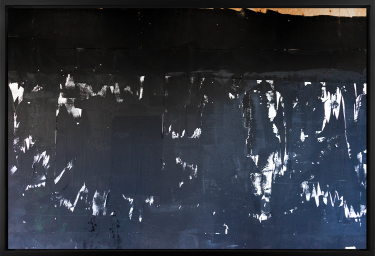 Color image of a large photograph of a black exterior wall with white paint splotches and wood covering its surface 