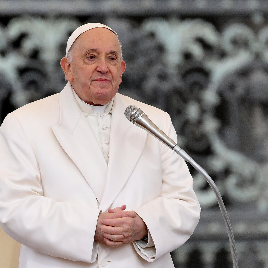 The pope, in a white suit, stands behind a microphone.
