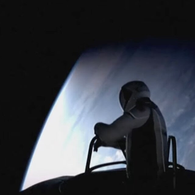 The top half of Jared Isaacman in a spacesuit outside a Crew Dragon capsule with Earth in the background.