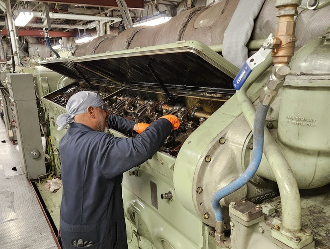 Person working on a large industrial ferry engine with its cover open