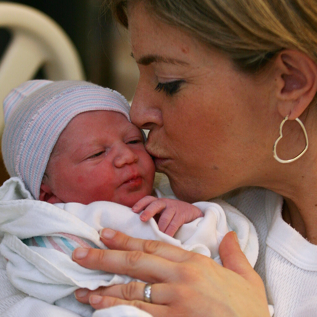 A woman kisses a newborn baby on the cheek.