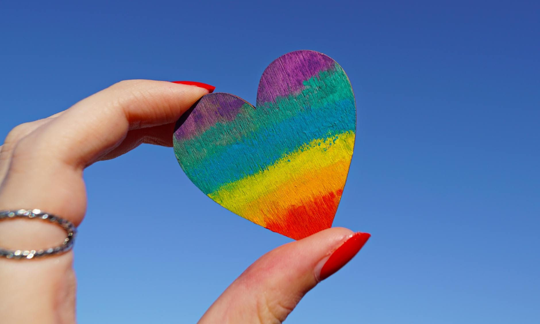A hand holding a rainbow coloured heart 