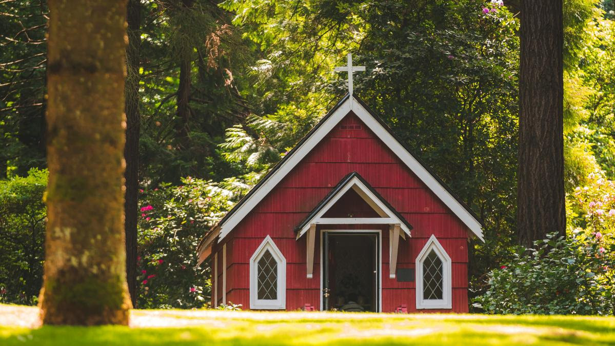 a small red church building surrounded by greenery