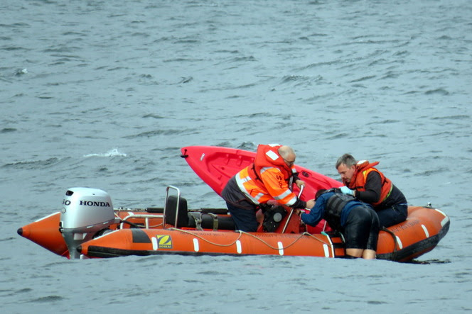 Two people n a rescue boat pulling a third person out of the water