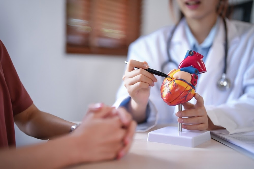 Asian cardiologist doctor women explaining about anatomical of human heart model to female patient after examining health while giving counseling about medical and mental health therapy in clinic.