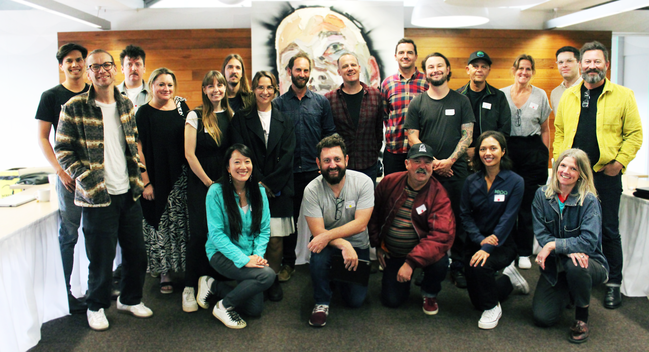 A group photo of 20 participants at the inaugural MPSA roundtable, smiling in front of a large painting and wood-paneled wall in a meeting room.