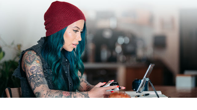 A woman with blue dyed hair plays a mobile game using an Xbox controller.