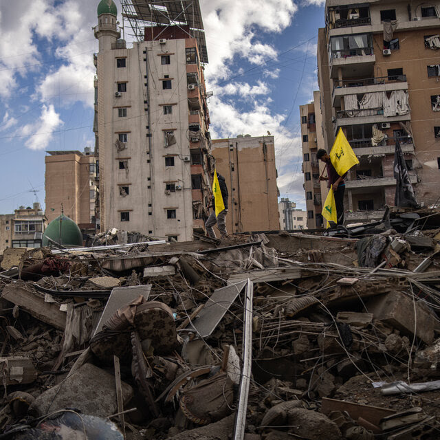 A man stands on a pile of debris holding yellow flags.