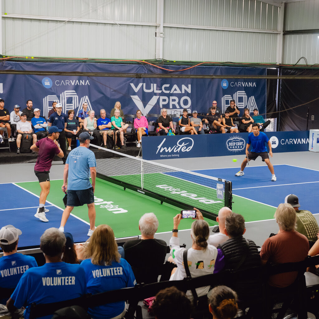 Four men playing pickleball in front of an audience.