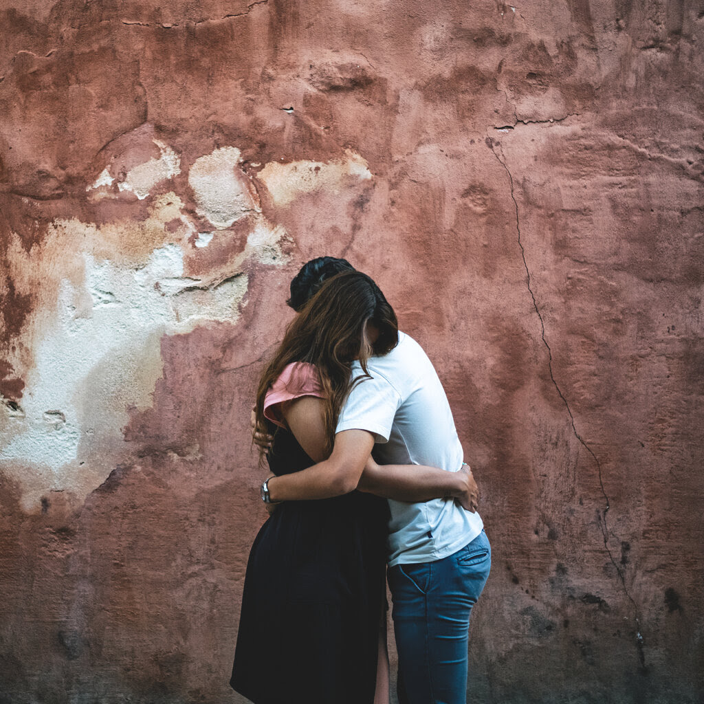 Luz and her son hug each other, with a stone wall behind them. 