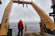 Two scientists stand under hydrolic pullies working to pull in the EcoFoci surface mooring