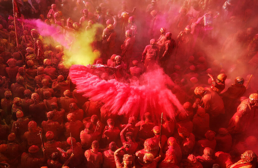 Celebrants are covered in red and pink hues outside a temple.