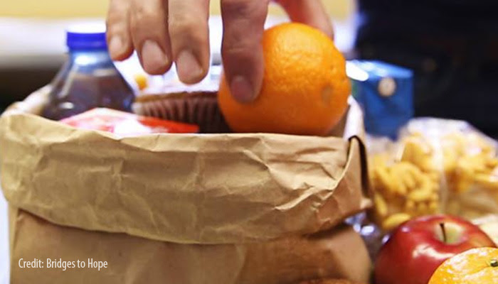 Orange being placed in a brown paper bag with other food items