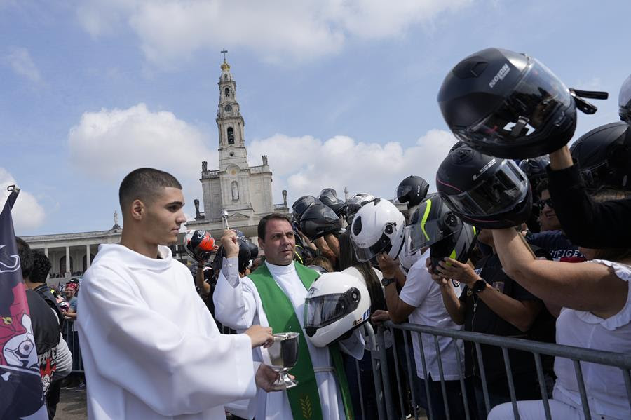 Motorcyclists hold their helmets up for a priest to bless with Holy Water.