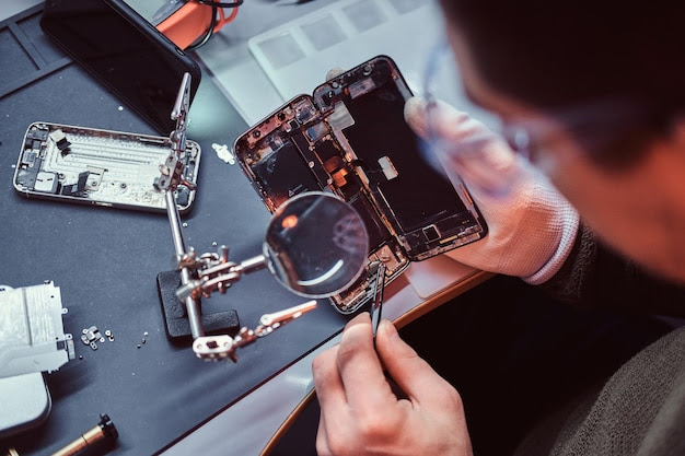 Repairman uses magnifier and tweezers to repair damaged smartphone. Close-up photo of a disassembled smartphone.