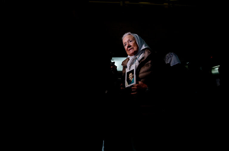 A portrait of a woman in a white kerchief holding a small photo of a man.