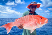 Man holds up a large red snapper on a sunny day on the ocean