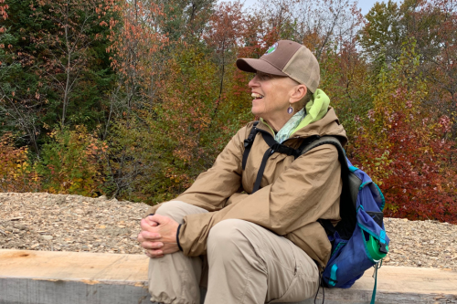 A white woman in a ballcap and hiking clothes is seated on a stone bench.