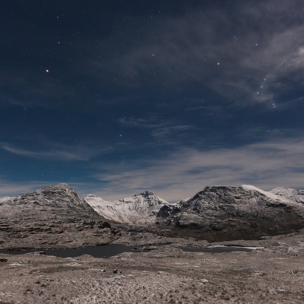 Low, gray mountains under a dark sky with wispy clouds.