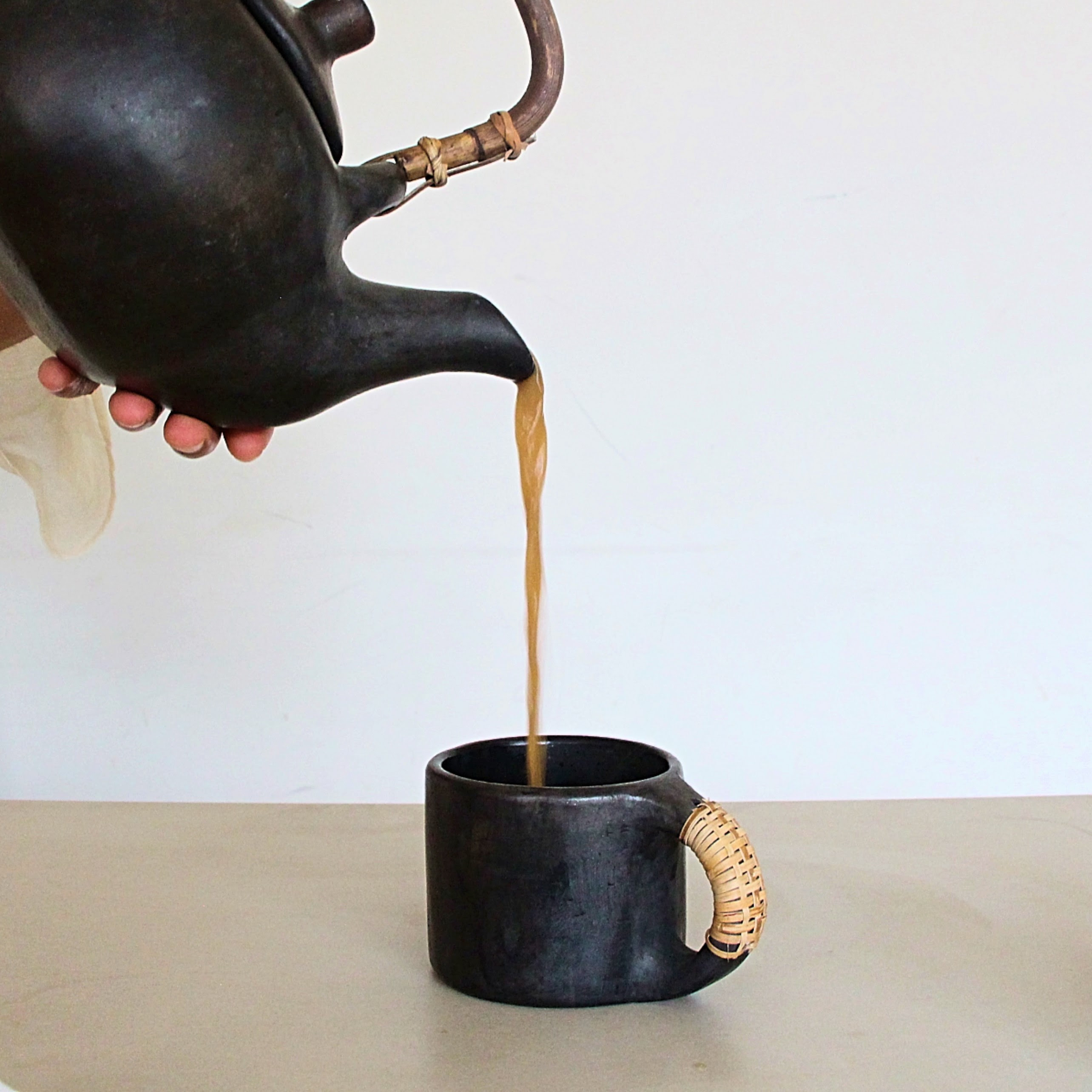 Tea being poured from a black teapot into a black mug