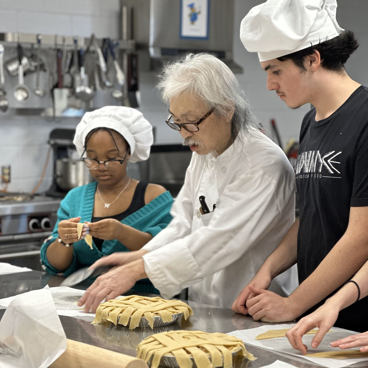 a culinary instructor shows two students a cooking technique inside a kitchen