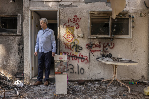 Yuval Bitton se tient debout, détournant le regard de la caméra, devant une maison avec des graffitis à l'extérieur.