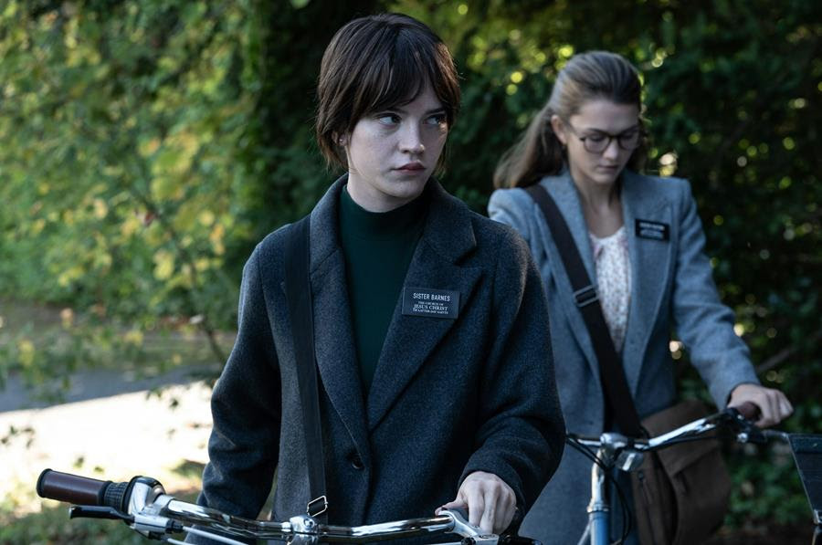 Two young women with black name tags attached to their coat lapels stand in front of trees.